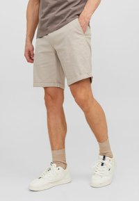 Pantalones cortos de algodón beige con dobladillos enrollados, bolsillos laterales, combinados con zapatillas blancas y calcetines beige. Diseño simple y ajuste relajado.
