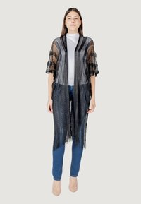 Sciarpa nera in pizzo con tessuto trasparente e orlo frangiato, design aperto, indossata sopra una maglietta bianca e jeans blu, con maniche corte.