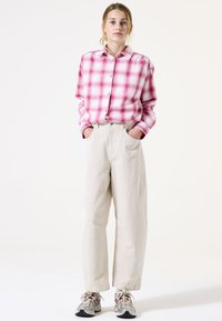 Camisa a cuadros en rosa y blanco, pantalones de pierna ancha color crema y zapatillas grises con acentos rojos. Tejido suave, ajuste relajado y diseño clásico.