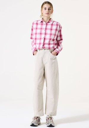 Camisa a cuadros en rosa y blanco, pantalones de pierna ancha color crema y zapatillas grises con acentos rojos. Tejido suave, ajuste relajado y diseño clásico.
