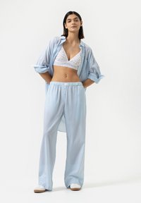 Lichtblauw gestreept overhemd met knopen, witte kanten bralette en bijpassende gestreepte broek; ontspannen pasvorm, zacht stof en eenvoudige witte instappers.