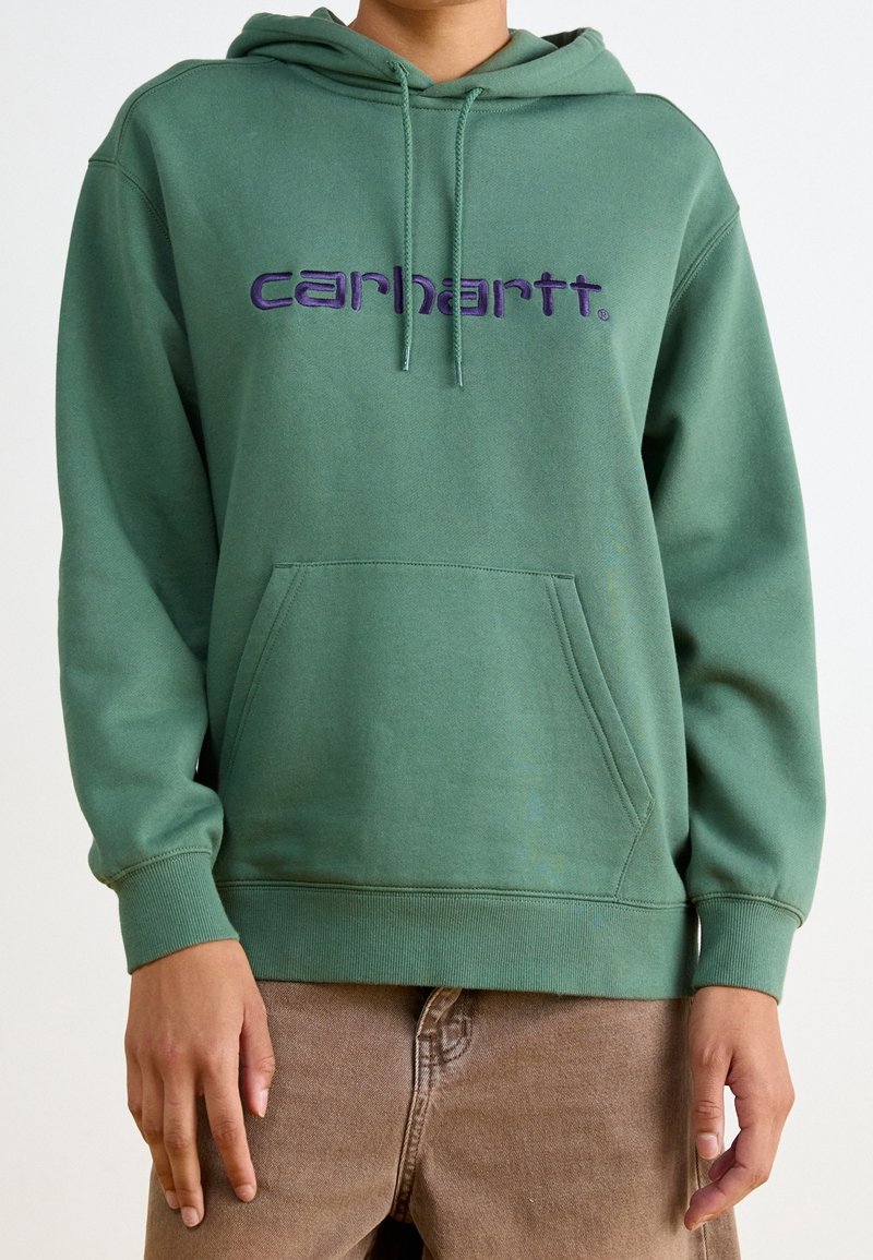 Zelená mikina s kapucí a přední kapsou, s fialovou vyšívanou značkou "carhartt". Má stahovací kapuci a žebrované manžety a lem.