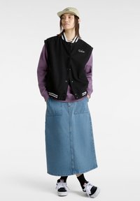 Chaqueta varsity negra con puños a rayas, sudadera morada debajo, falda de mezclilla azul y zapatillas negras con acentos blancos.
