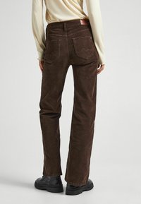 Bruine corduroy broek met een rechte pijp, voorzien van twee achterzakken en een leren logo label op de tailleband. Getextureerd oppervlak.