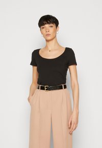 Camiseta negra de manga corta y escote redondo combinada con pantalones de tiro alto rosa claro, ajustados con un cinturón negro con hebilla dorada.