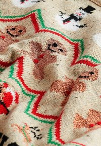Tkana tkanina z świątecznym wzorem przedstawiającym pierniczki, bałwanki i akcenty świąteczne w kolorach czerwonym, zielonym i czarnym na beżowym tle.