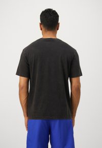 Mørkegrå bomulls t-skjorte med korte ermer, rund hals, og en litt falmet finish, brukt sammen med blå shorts. Minimalistisk design.