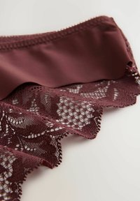 Bordo grudnjak s čipkastim obrubom s cvjetnim uzorkom, glatka tkanina i valoviti rubovi, pružajući nježnu teksturalnu kontrast.