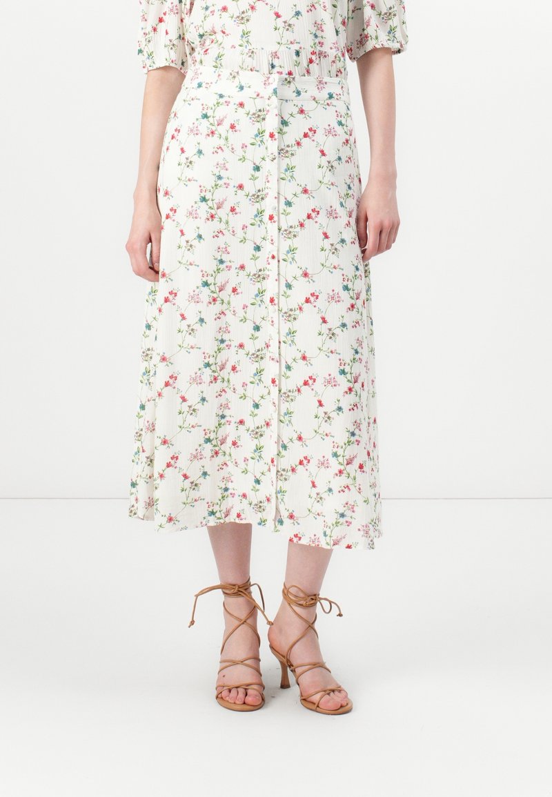 Robe midi blanche à imprimé floral rose, rouge et vert, manches bouffantes, boutons sur le devant, portée avec des sandales à talons marron à brides.