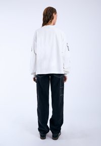 White oversized long-sleeve shirt with a crew neckline, paired with black baggy pants featuring side pockets and contrasting stitching.