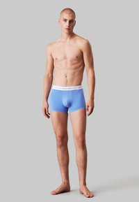 Boxer elastici blu da uomo con vita elastica bianca, texture liscia e design aderente. Nessun motivo o accento visibili.