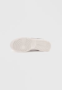 Sola de sapatilha Nike em borracha branca com um padrão de pisada circular e linhas gravadas, com uma marcação mínima visível.