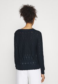 Tmavě námořnický pletený svetr s volným, texturovaným designem, kulatým výstřihem a žebrovaným lemem. Dlouhé rukávy s pohodlným střihem.