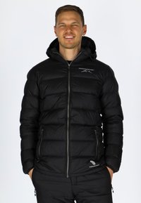 Svart puffjacka med huva, med quiltad textur, fickor med dragkedja och en logga på övre vänster sida. Lätt och isolerad design.