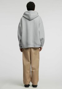 Grå hettegenser med romslig passform, stor hette og ribbestrikkede mansjetter, kombinert med beige vide bukser og svarte sko. Jevn stofftekstur.