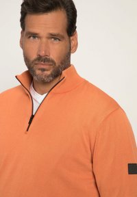 Pullover arancione con collo a mezza zip, tessuto testurizzato e un accento nero sulla manica. Presenta una vestibilità classica e una finitura liscia.