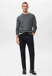 Mörkgrå stickad tröja, svarta byxor och svarta skor. Tröjan har en rundad halsringning; byxorna är skräddarsydda med rak passform.