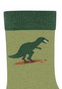 Grüne Socken mit einem pixelierten Dinosaurierdesign in Dunkelgrün, mit einem roten Punkt unter dem Dinosaurier, auf einem hellgrünen Hintergrund.