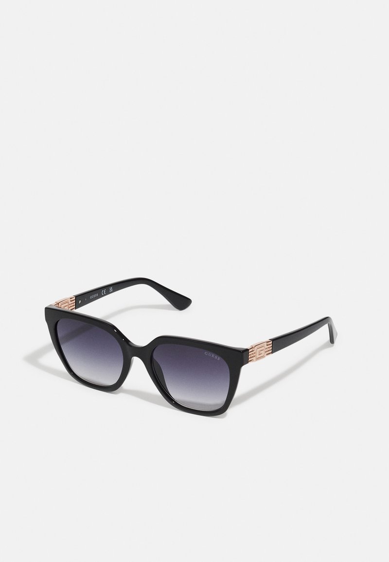 Black sunglasses with a geometric frame, gradient gray lenses, and rose gold hardware accents on the temple featuring a logo pattern.