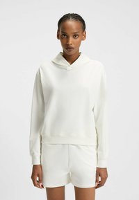 Vaalean ivory-hoodie, jossa on pehmeä pinta, leveä kaula-aukko ja ribbaavat hihansuut. Rintaan on painettu pieni logo. Yhdistettyinä vastaaviin shortseihin.