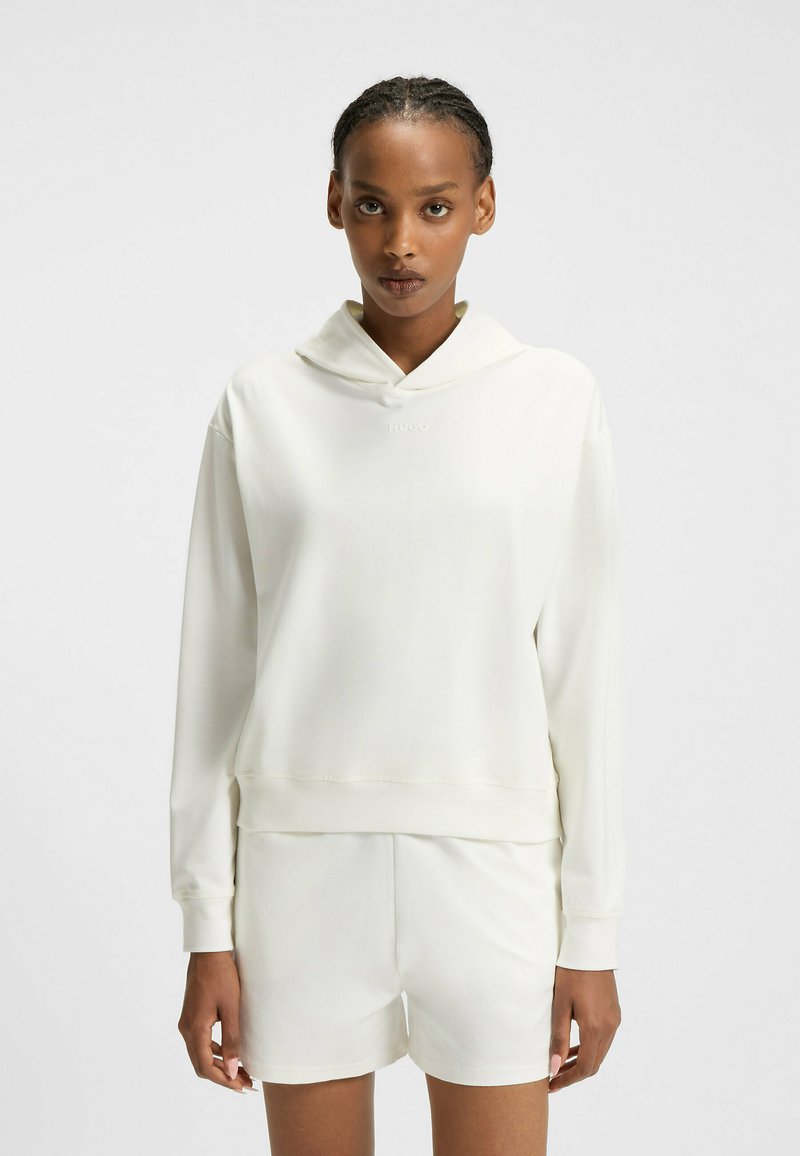 Licht ivoorkleurige hoodie met een zachte textuur, een brede halslijn en geribbelde mouwen. Kenmerkt zich door een klein logo op de borst. Gecombineerd met bijpassende shorts.
