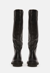 Bottes jusqu'aux genoux en cuir noir avec une texture lisse et un bout arrondi. Elles présentent un talon bas empilé et des détails de couture subtils le long des côtés.