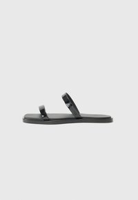 Mustat flip-flop-sandaalit, joissa on kaksi kiiltävää, tasaista remmiä ja teksturoitu, matta pohja. Moderni, minimalistinen muotoilu, joka sopii rentoon käyttöön.