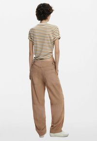 Randig kortärmad skjorta i beige och brunt med upprullade ärmar; löst sittande beiga byxor med fickor och en knappdetalj vid midjan.