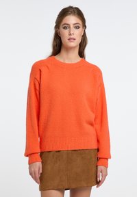 Maglione a maglia arancione brillante con una vestibilità rilassata, polsini e orlo a costine, e tessuto testurizzato. Indossato con una mini gonna in suede marrone.