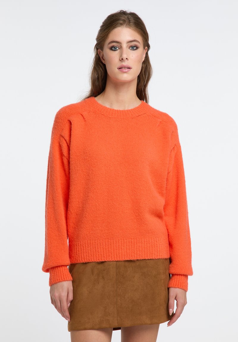 Maglione a maglia arancione brillante con una vestibilità rilassata, polsini e orlo a costine, e tessuto testurizzato. Indossato con una mini gonna in suede marrone.