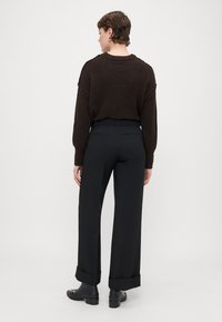 Brown textured sweater paired with black wide-leg trousers, featuring rolled cuffs and back pockets, worn with black ankle boots.