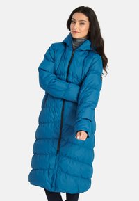 Lange pufferjas in felblauw, gemaakt van gewatteerde stof, met een hoge kraag, ritssluiting en zwarte accenten op de ritssluiting en manchet.