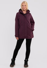 Lilla vandtæt jakke med hætte, frontlynlås, to sidelommer og justerbare manchetter, parret med sorte leggings og støvler.