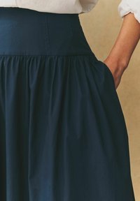 Jupe bleu marine avec une taille haute élastique et un tissu froncé. Comprend des poches latérales et une texture lisse et douce.