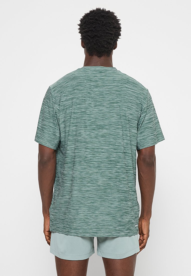 Camiseta corta de manga verde con textura, que presenta un cuello redondo y un corte relajado. Se lleva con pantalones cortos de color gris claro.