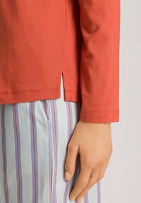 Top de manga larga color coral con detalle de abertura lateral, combinado con pantalones de rayas verticales en azul claro. Textura de tela suave.