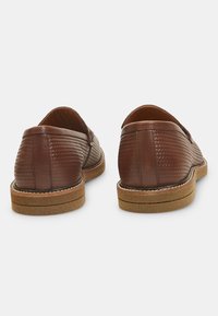 Zapatos de cuero marrón con un patrón de tejido texturizado y una suela de goma marrón claro, con un acabado suave y costuras contrastantes.