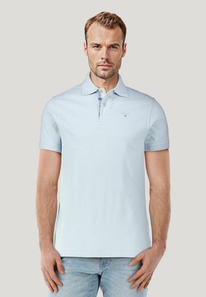 Lichtblauwe polo met een platte kraag, korte mouwen en een patroonaccent onder de kraag. Soepele textuur, geen zichtbaar logo.