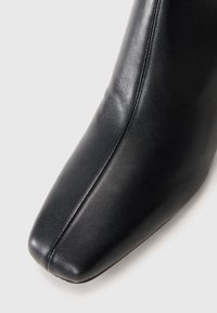 Stivaletto in pelle nera, con punta quadrata, texture liscia e un design pulito e minimalista, caratterizzato da dettagli di cucitura laterale.