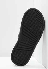 Sort skosål med tekstureret gummioverflade, prydet med et logo og et mønstret grebdesign for bedre traction.