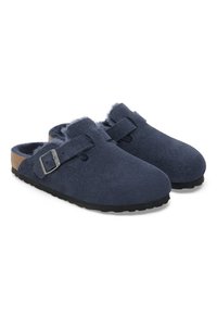 Marineblaue Wildleder-Clogs mit rundem Zehenbereich, verstellbarem Riemen mit metallischer Schnalle und weichem Innenfutter. Schwarze Gummisohle mit strukturiertem Grip.