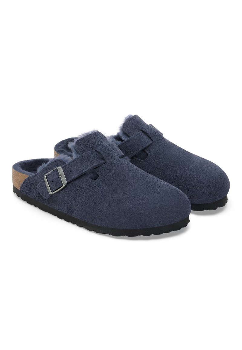 Marineblaue Wildleder-Clogs mit rundem Zehenbereich, verstellbarem Riemen mit metallischer Schnalle und weichem Innenfutter. Schwarze Gummisohle mit strukturiertem Grip.