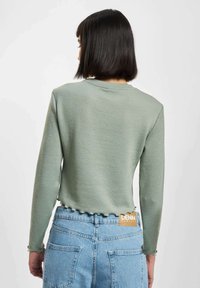 Grønn ribbet strikket langermet topp med bølget kantdetalj, sammen med høy midje lys blå denimshorts med logo-tag.