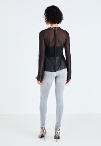 Črna prosojna bluza z dolgimi rokavi in ruffled robom, v kombinaciji s svetlo sivimi kavbojkami. Zadaj ima srednjo šiv in nežno gumbasto zapiranje.