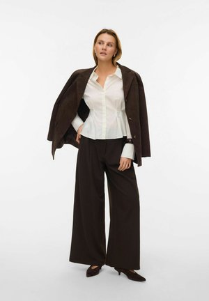 Biała koszula na guziki z baskinką w talii, brązowa zamszowa kurtka zarzucona na ramiona, szerokie ciemne spodnie i ciemne buty w szpic.