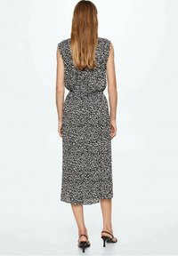 Černobíle vzorované šaty bez rukávů s přiléhavým pasem, splývavou sukní a délkou ke kolenům, doplněné o černé sandály na podpatku.