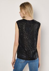 Zwart mouwloos topje bedekt met pailletten, met een ronde halslijn en een gladde textuur. Gecombineerd met een blauwe spijkerbroek, heeft de outfit een casual uitstraling.