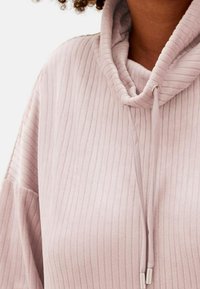 Pullover a coste rosa chiaro con collo a cappuccio, dotato di lacci e dettagli in metallo argentato. Tessuto morbido con una vestibilità rilassata.