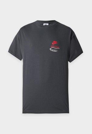 Σκούρο γκρι κοντομάνικο Nike T-shirt με κόκκινο κείμενο "Nike Arts Club" και λευκό γραφικό στο αριστερό στήθος.
