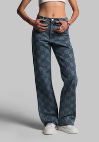 Wide-leg denim jeans with a faded blue wash, featuring a repeating light blue logo pattern, classic five-pocket design, and metallic button closure.